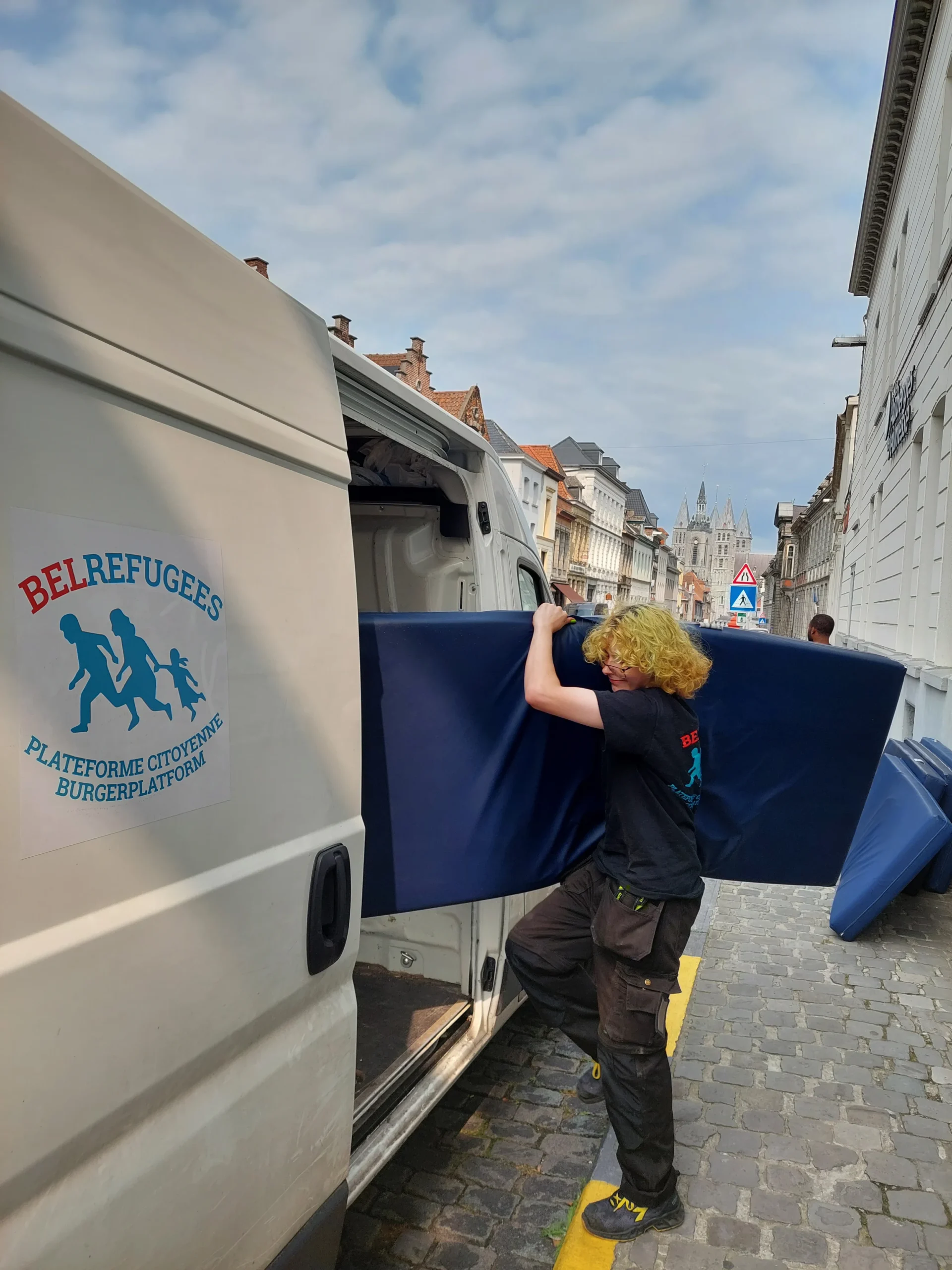 đ€ BelRefugees 4 Une personne entrain de chargĂ© une camionnette arborant le logo BelRefugge avec un matelas bleu