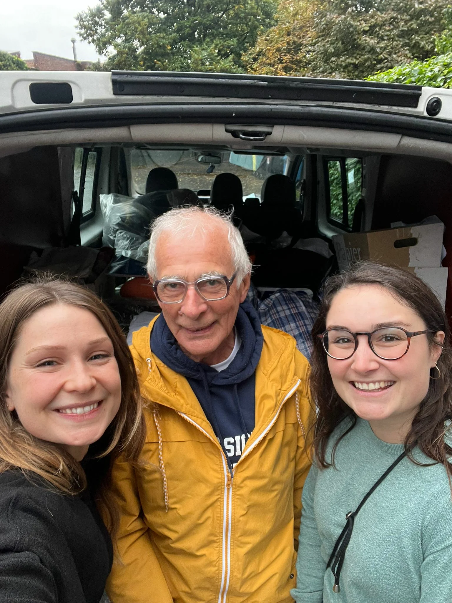 🕊️ Say Hi For Peace 2023 5 Un homme âgé avec à sa gauche et à sa droite deux jeunes filles souriantes devant une voiture remplie de dons